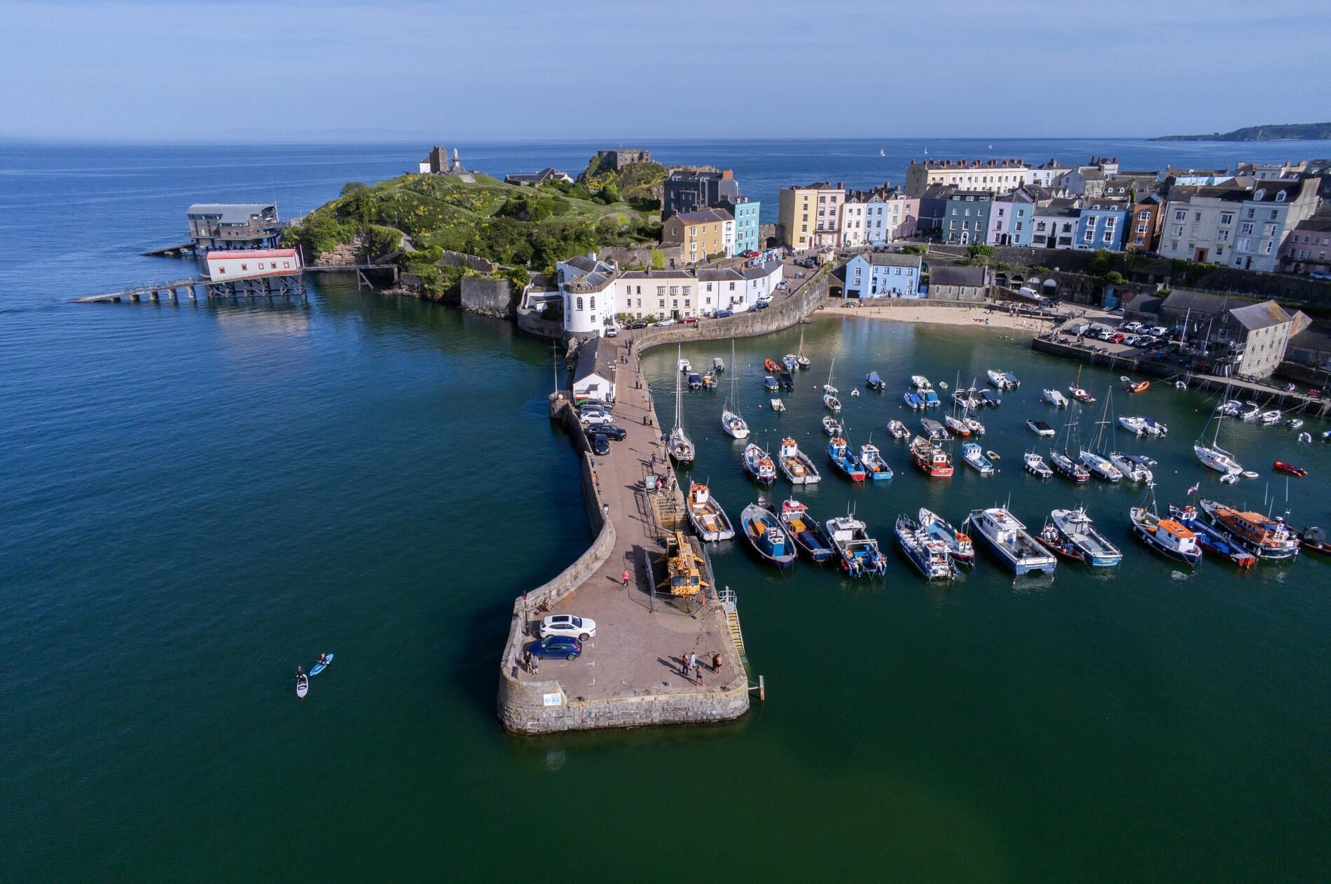 An aerial view of a coastal town with a historic fort, colorful buildings, and a marina with numerous boats.