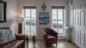 A cozy room with a brown leather sofa, a glass coffee table, a brown leather armchair, and a poster of a coastal scene.