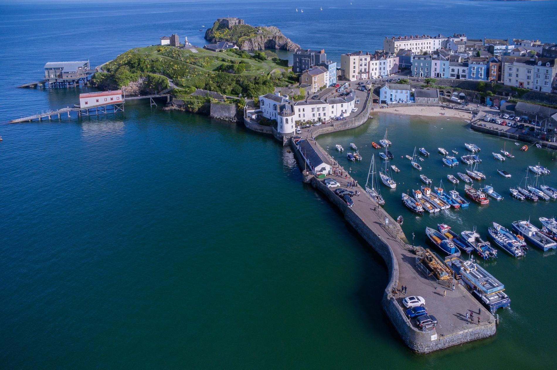 An aerial view of a coastal town with a fortified harbor, historic buildings, and a lighthouse.