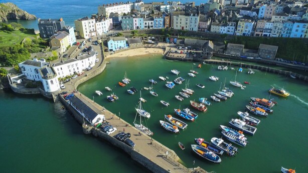 A coastal town with a marina filled with boats, historic buildings, and a clear view of the sea.