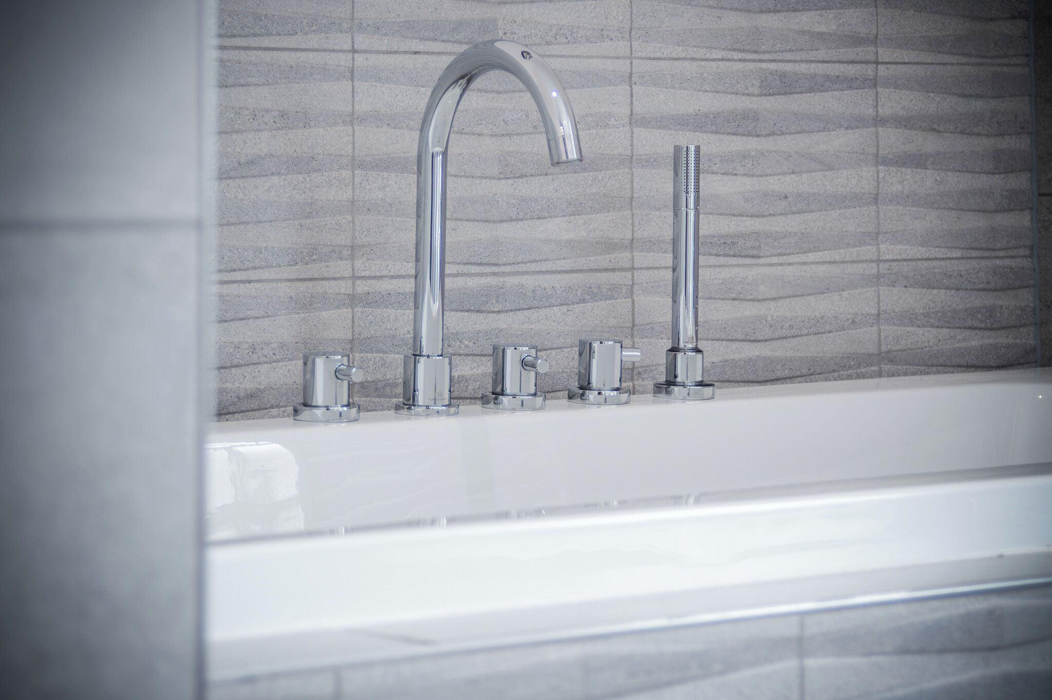 A modern bathroom with a white bathtub, a curved faucet, and a vertical showerhead.