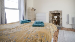 Une chambre à coucher avec un grand lit, une cheminée en pierre, un radiateur blanc et une fenêtre avec des rideaux.