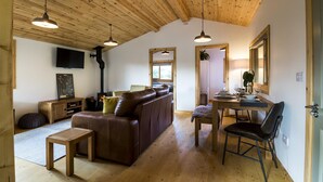 A cozy living room with a wooden ceiling, a leather sofa, a dining table with chairs, and a fireplace.