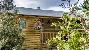 A log cabin with a wooden deck, a window with a hanging plant, and a sign that reads "LAUREL".