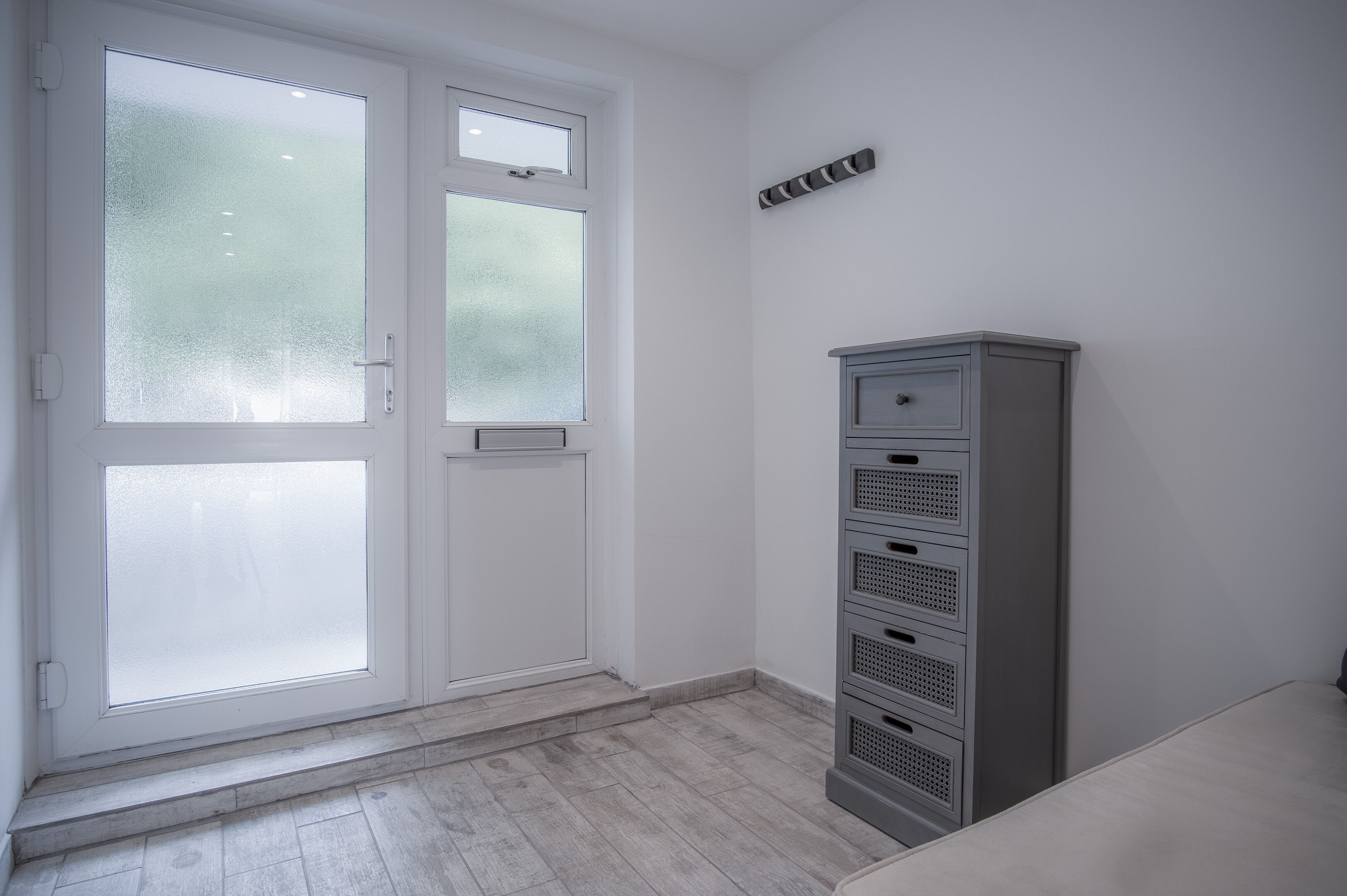 Ein Zimmer mit einer weißen Tür, die mit gefrosteten Glasscheiben versehen ist, einem grauen Aktenschrank und einer kleinen Stufe zum Eingang.