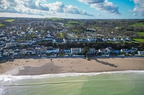 A coastal town with a beach, houses, and a hilly landscape in the background.