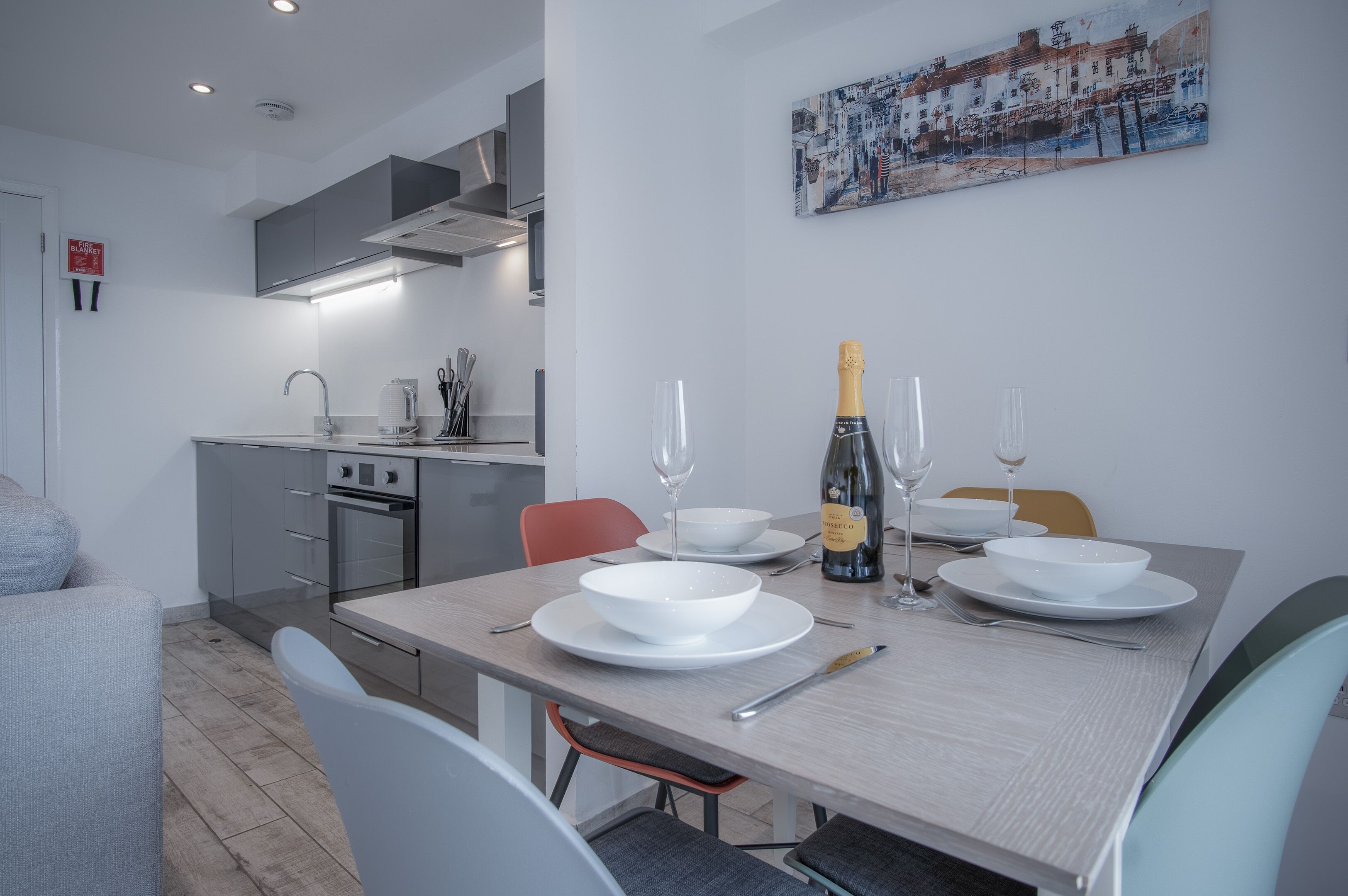 A modern kitchen with a dining area, a painting on the wall, and a bottle of champagne on the table.