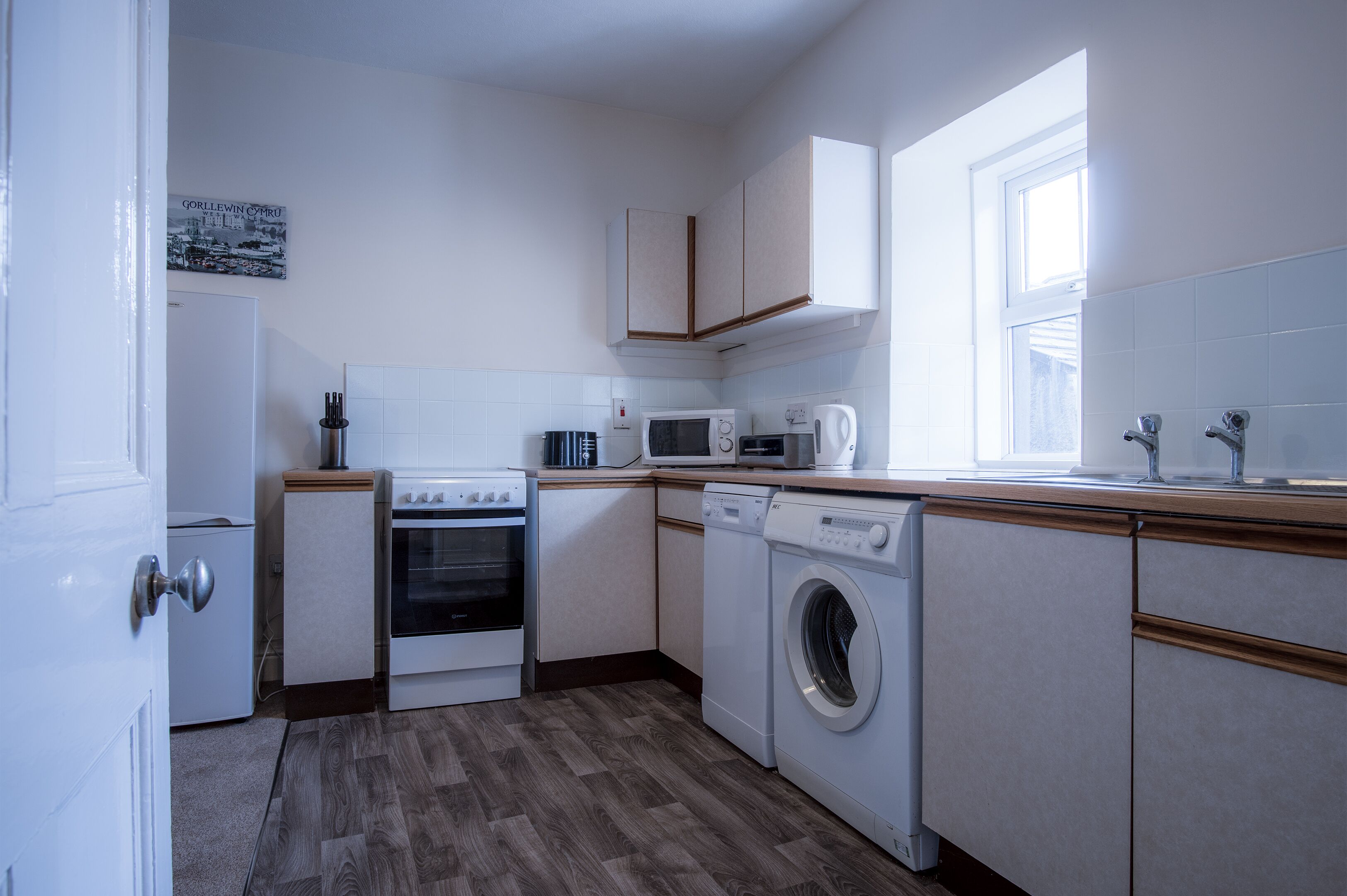 Eine kompakte Küche mit weißen Geräten, darunter Mikrowelle, Backofen und Waschmaschine, und ein Fenster für natürliches Licht.
