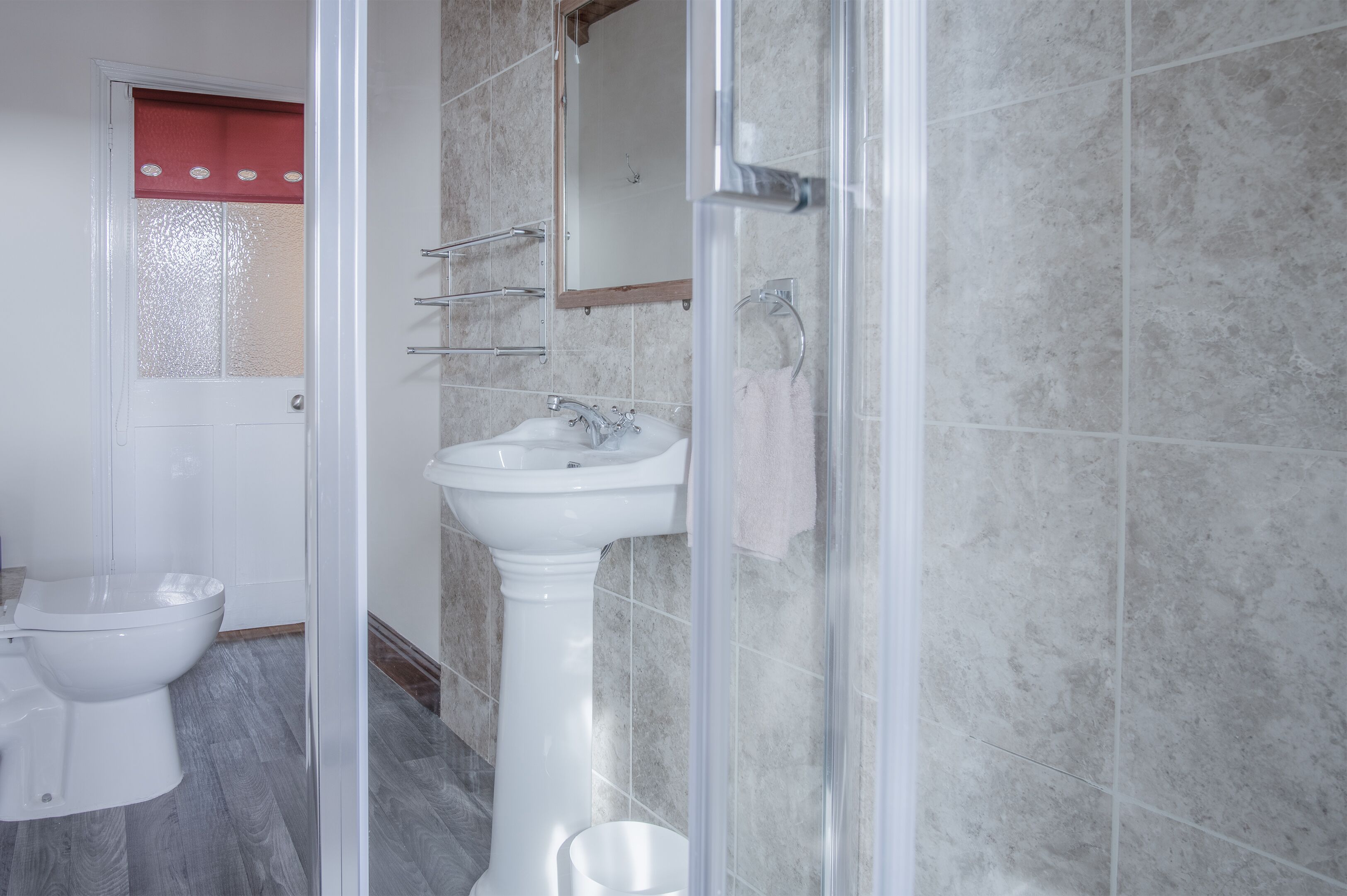 A bathroom with a white toilet, a pedestal sink, and a glass shower enclosure.