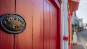 A red door with a metal plaque that reads "Dragons Den." - Dragons Den - 2 Bedroom Apartment - Tenby (Tenby)