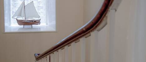 A staircase with white railings and a window with a sailboat model.