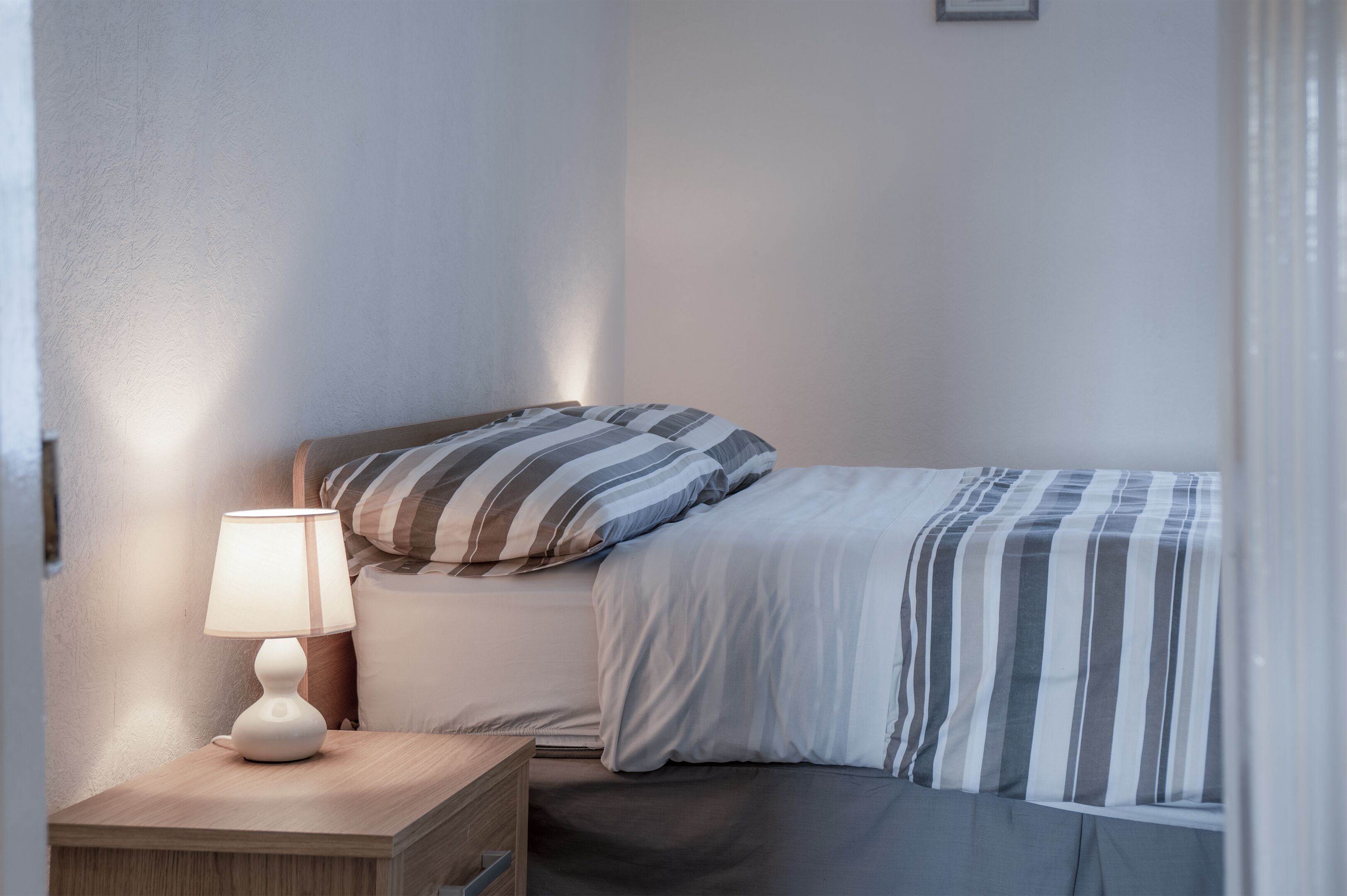 A neatly made bed with striped bedding, a bedside lamp, and a wooden nightstand.