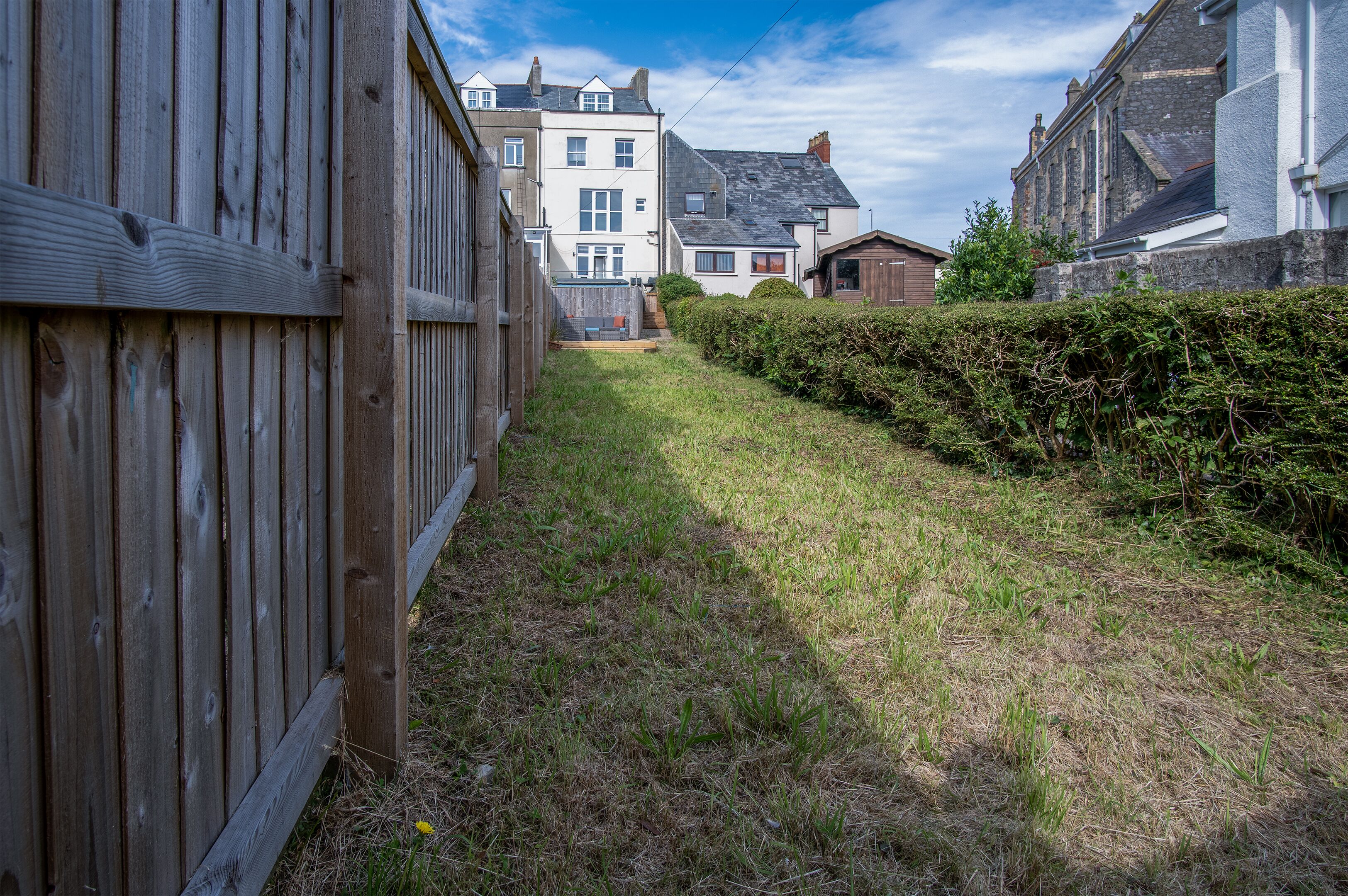 Ein schmaler Pfad führt zu einem Gebäude im traditionellen Stil, umgeben von einem Holzzaun und einer Hecke.