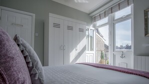 Ein Schlafzimmer mit einem großen Bett, einem weißen Kleiderschrank und Blick ins Freie durch ein Fenster.