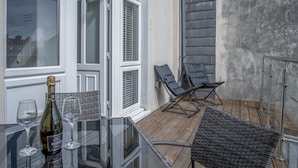 Ein Balkon mit Glastisch, zwei Stühlen und einer Champagnerflasche.