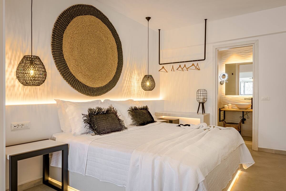 Quarto moderno com cama grande, mesas de cabeceira, luminária pendente e espelho.