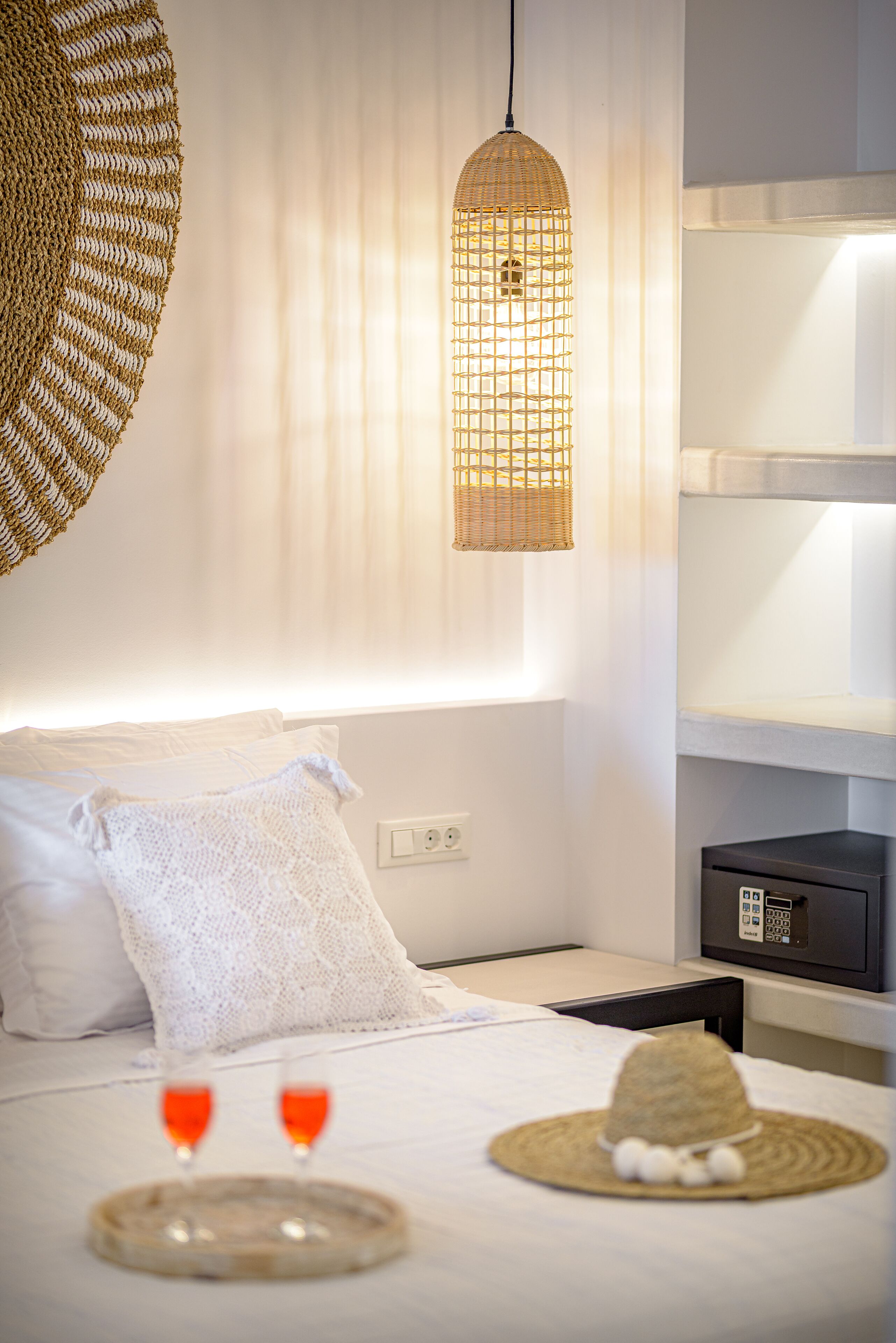 Una cama bien hecha con sábanas blancas, una lámpara de fibra trenzada arriba y un pequeño electrodoméstico negro en la mesita.