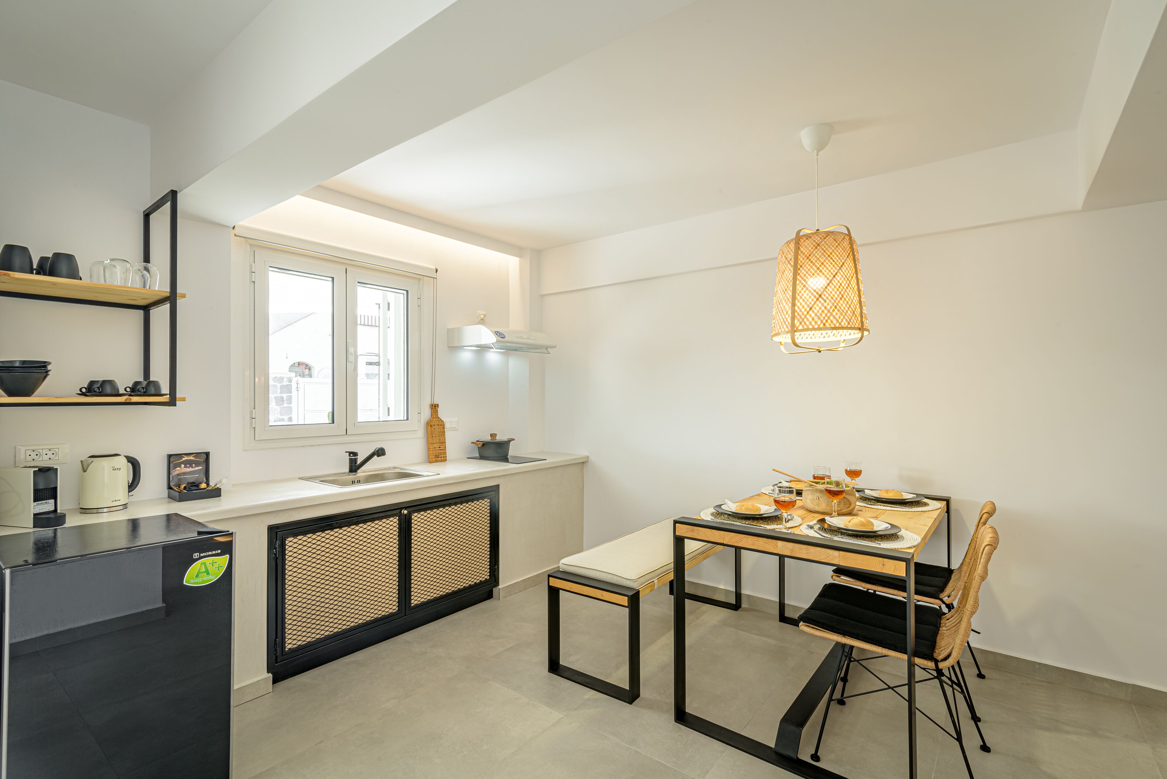 Una cocina moderna con comedor, que incluye un refrigerador negro, una mesa de madera y una lámpara colgante de mimbre.