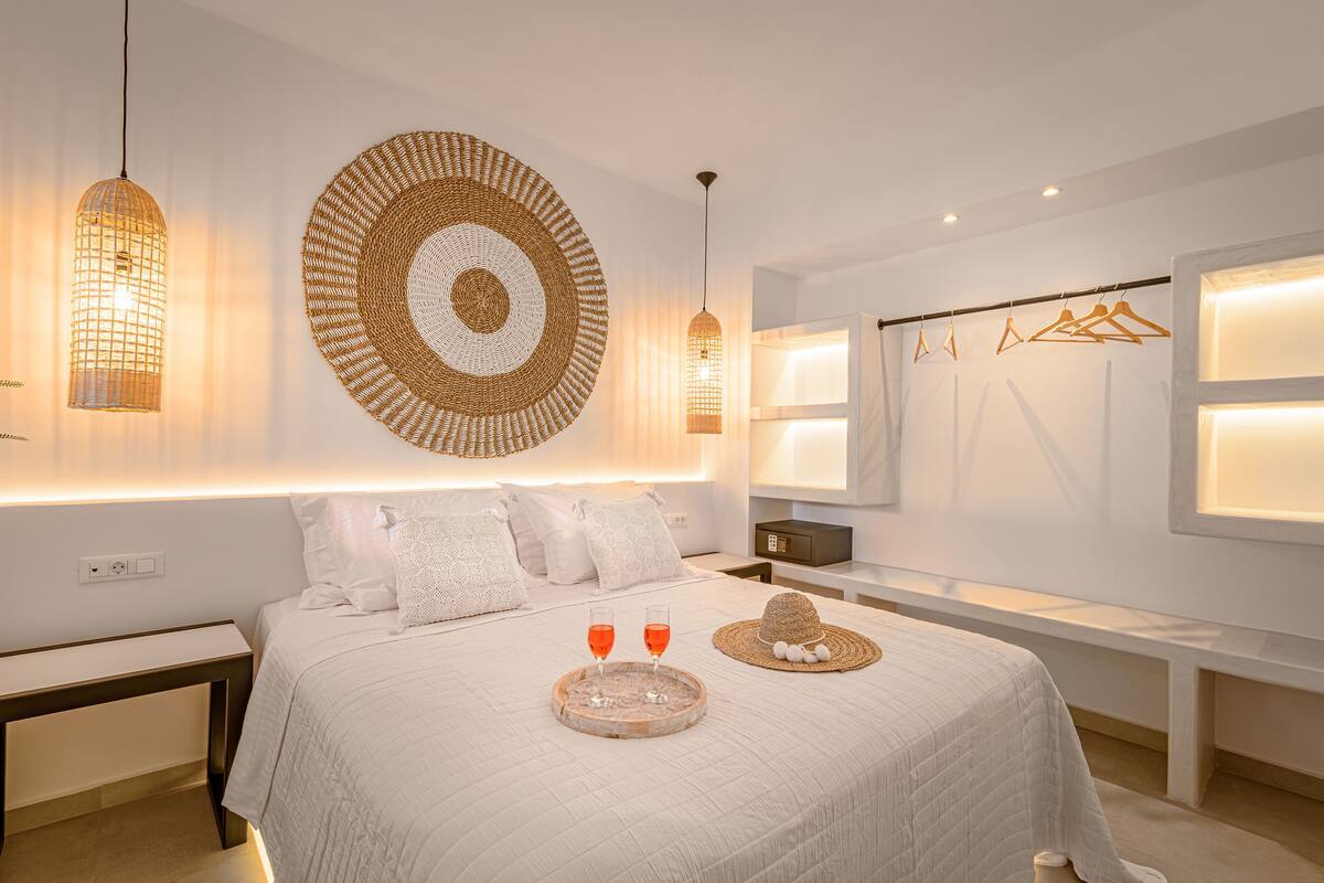 Quarto moderno com uma cama grande, mesas de cabeceira, abajur e uma obra de arte circular trançada na parede.