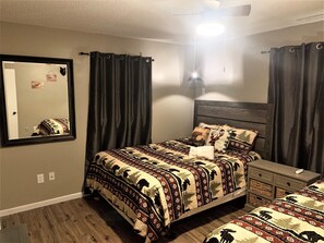 Ein Schlafzimmer mit einem großen Bett, einem Nachttisch, einer Kommode, einem Spiegel und dunklen Vorhängen.