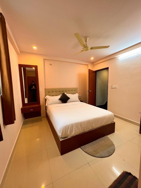 A hotel room with a bed, a nightstand, a mirror, a ceiling fan, and a door.