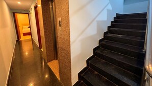 A modern hotel hallway with a polished black staircase, a marble wall, and a door leading to a room. - Hotel InTourist by Agira Hotel (Bengaluru)