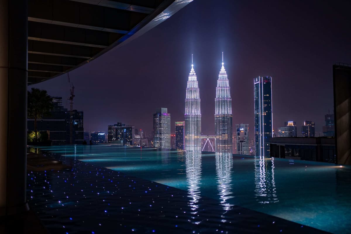 A nighttime view of a cityscape with two prominent skyscrapers, a bridge, and a body of water reflecting the lights.