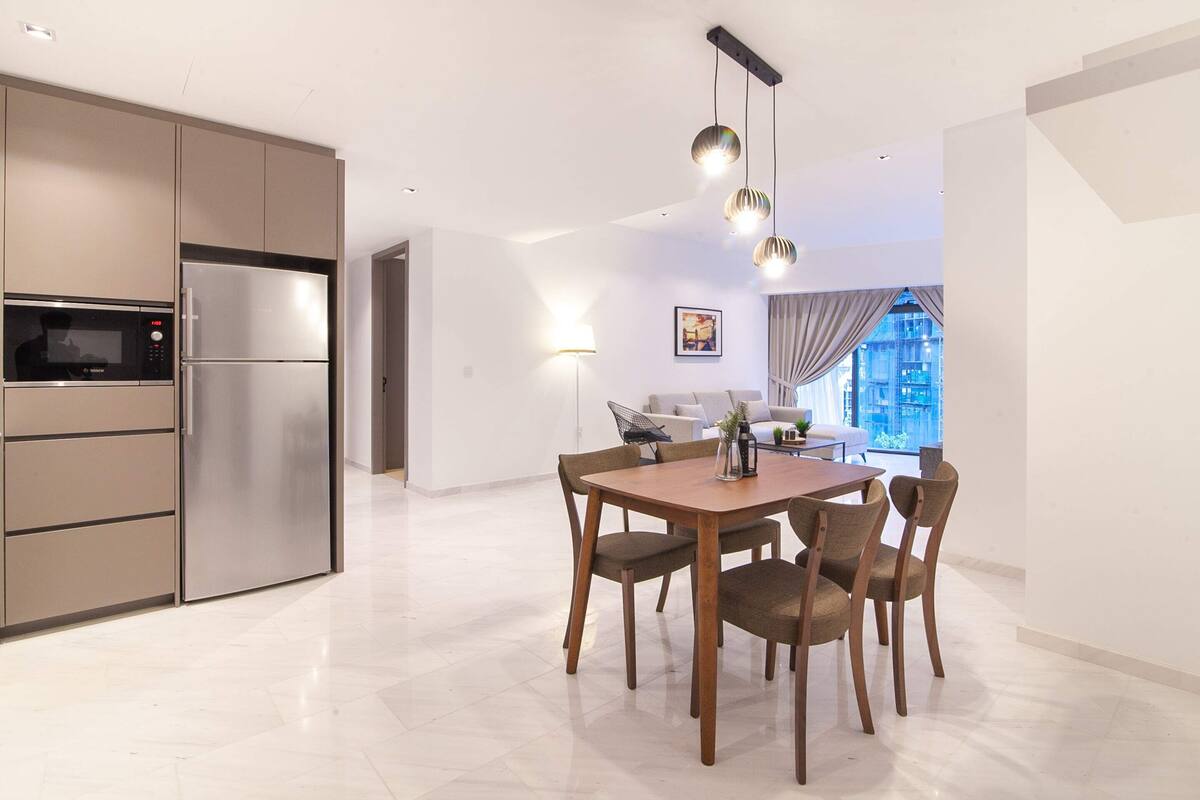 A modern kitchen with a built-in microwave and refrigerator, a dining area with a wooden table and chairs, and a view of the city through large windows.