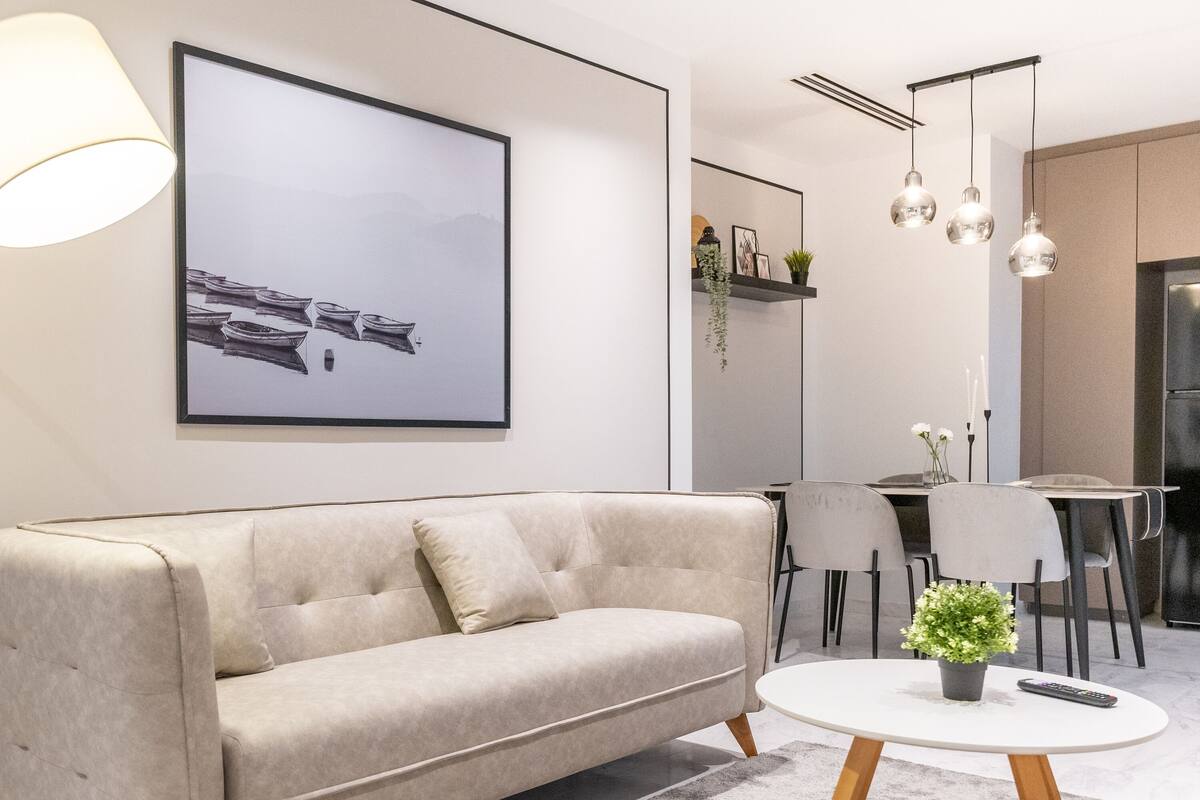 A modern living room with a sofa, a round coffee table, a framed picture, and a dining area with chairs and a table.