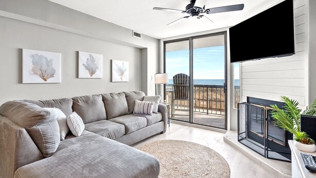 A modern living room with a grey sectional sofa, a round rug, and a balcony with a TV. - Welcome to WATER POINTE II, your ideal oceanfront escape in North Myrtle Beach (North Myrtle Beach)
