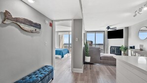 A modern living room with a grey sofa, a blue bench, a flat-screen TV, and a ceiling fan. - Welcome to WATER POINTE II, your ideal oceanfront escape in North Myrtle Beach (North Myrtle Beach)