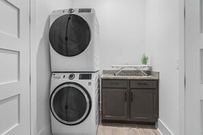 A laundry area with stacked washing machines and a countertop with an iron. - Luxury boulevard home w/private pool, outdoor kitchen-absolute heaven! (North Myrtle Beach)