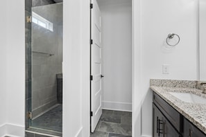 Un baño moderno con cabina de ducha de vidrio, paredes blancas y encimera de granito.