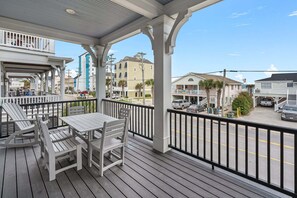 A covered outdoor seating area with a table and chairs, overlooking a street with parked cars and buildings. - Luxury boulevard home w/private pool, outdoor kitchen-absolute heaven! (North Myrtle Beach)