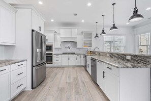 A modern kitchen with white cabinetry, stainless steel appliances, and a marble countertop.