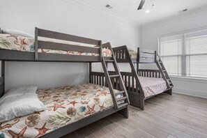 A room with two bunk beds, wooden flooring, and a large window with blinds.