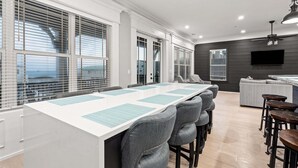 Een moderne vergaderruimte met een lange tafel, grijze gestoffeerde stoelen en een bar met krukken.