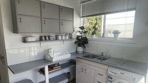 Cocina compacta con armarios blancos, lavavajillas integrado y ventana con vistas a zonas verdes.