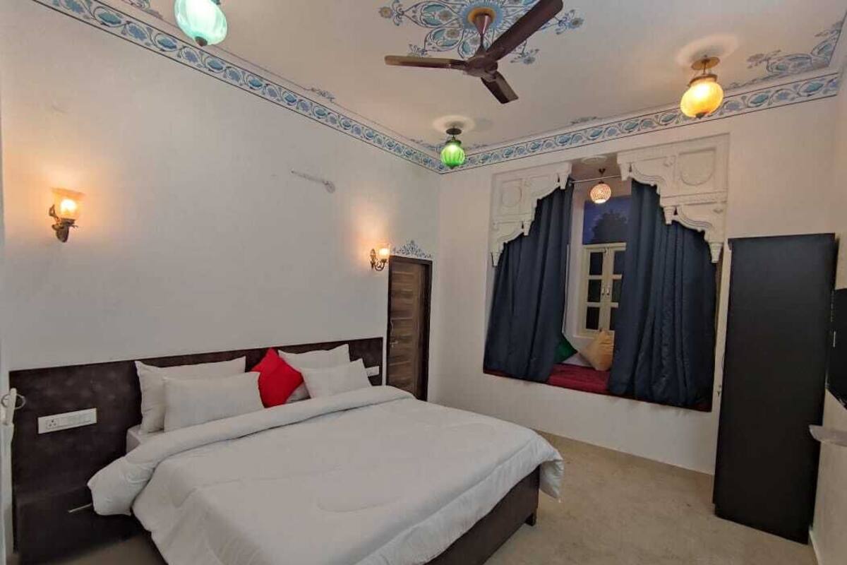 A bedroom with a bed, a ceiling fan, wall sconces, and a window with curtains.