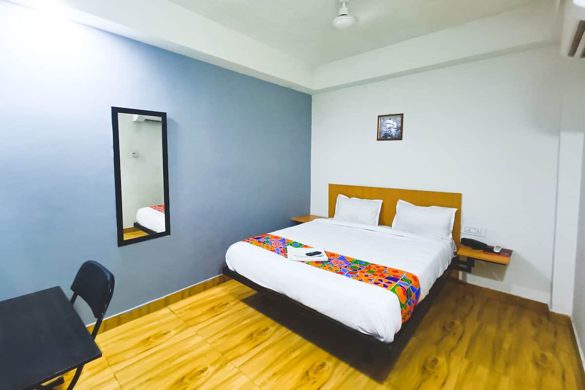A hotel room with a bed, a desk, a chair, a mirror, and a nightstand.