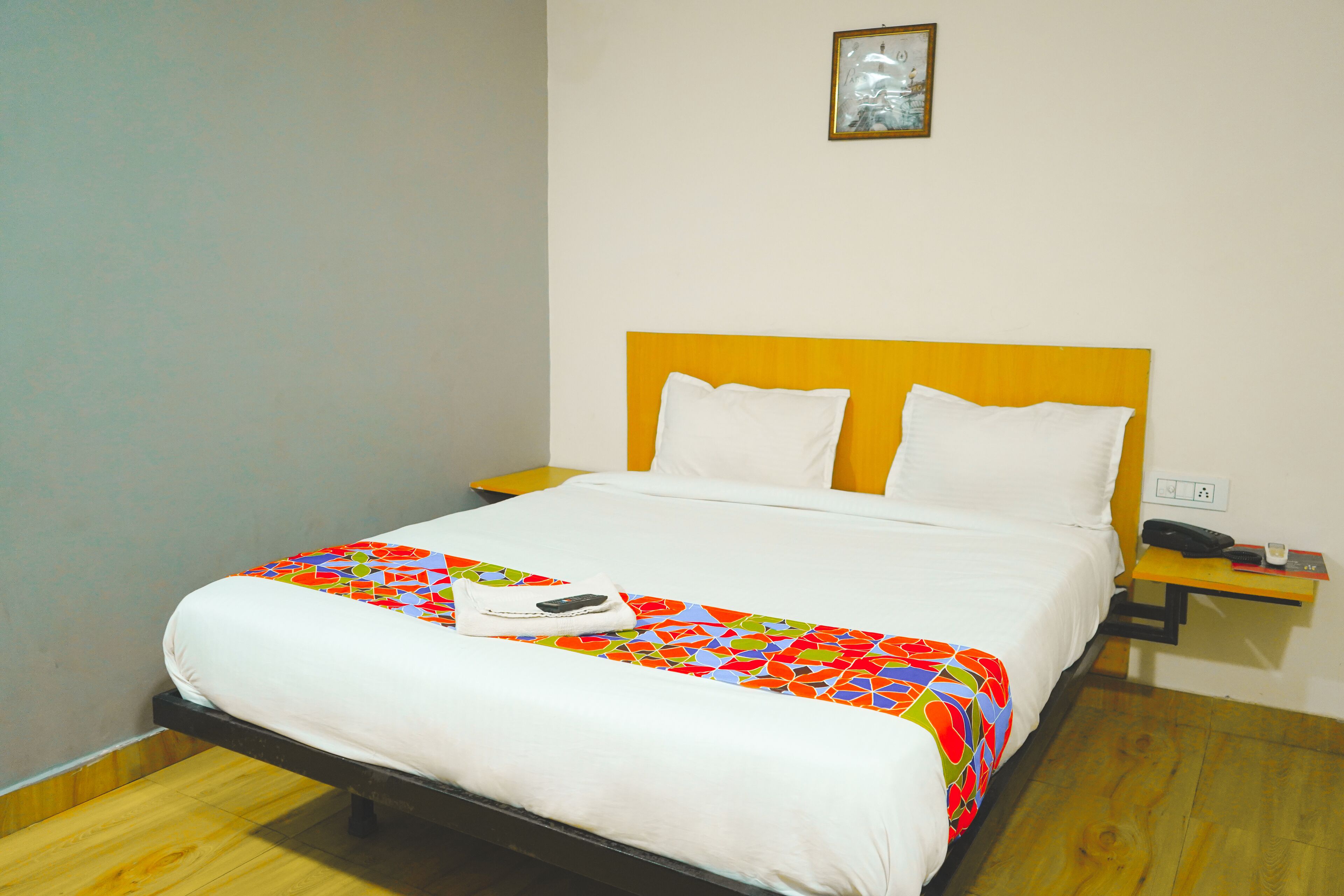 Una cama bien hecha con un colorido edredón de estampado geométrico, almohadas blancas y una mesita de noche con un teléfono y un control remoto.