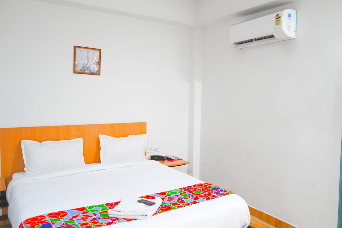 A hotel room with a bed, a nightstand, a phone, and an air conditioning unit.