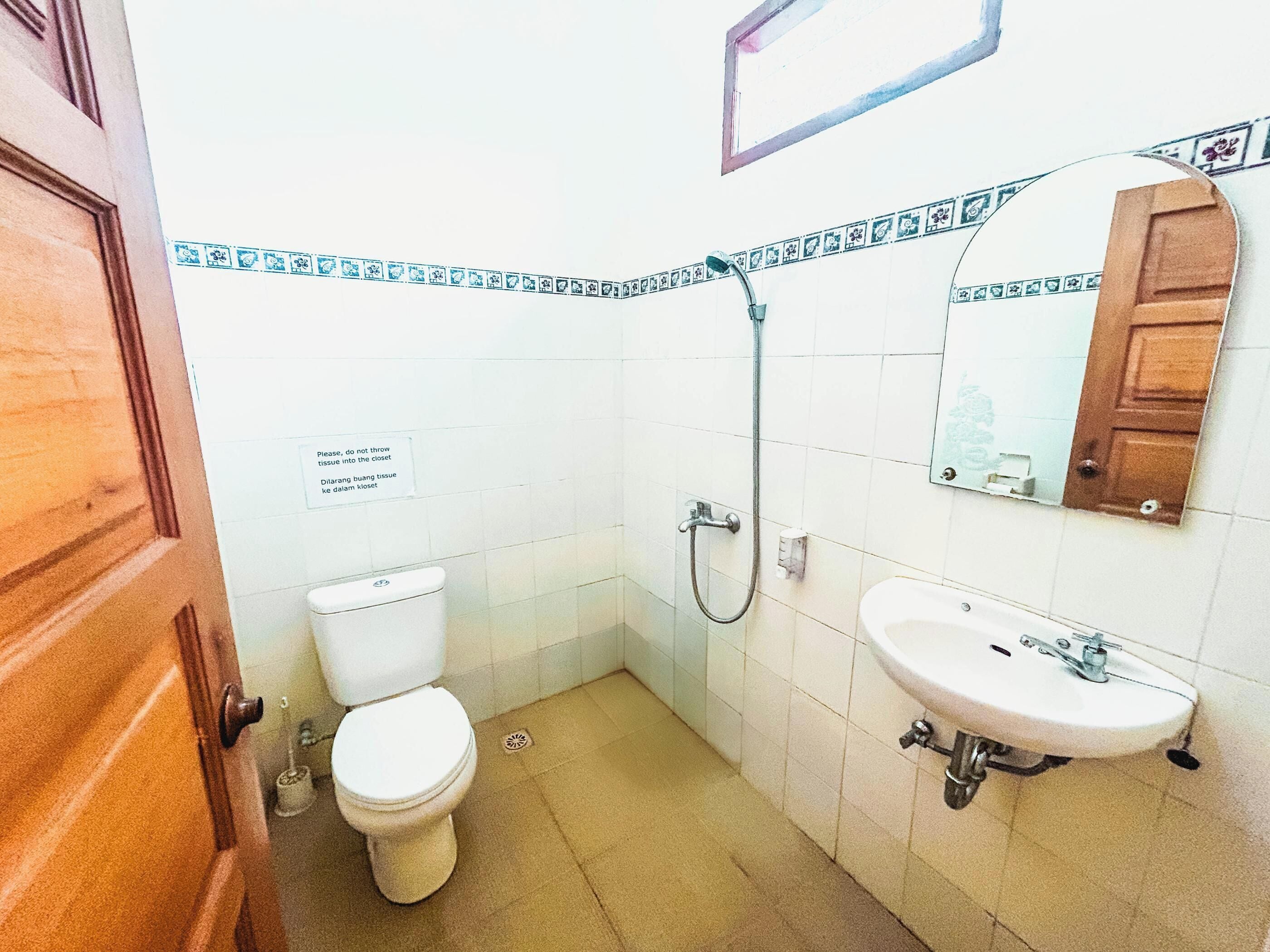 Un baño pequeño con inodoro, lavamanos y ducha. Hay un cartel en la pared y una puerta de madera.
