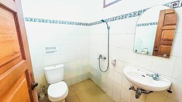 Un baño pequeño con inodoro, lavamanos y ducha. Hay un cartel en la pared y una puerta de madera.