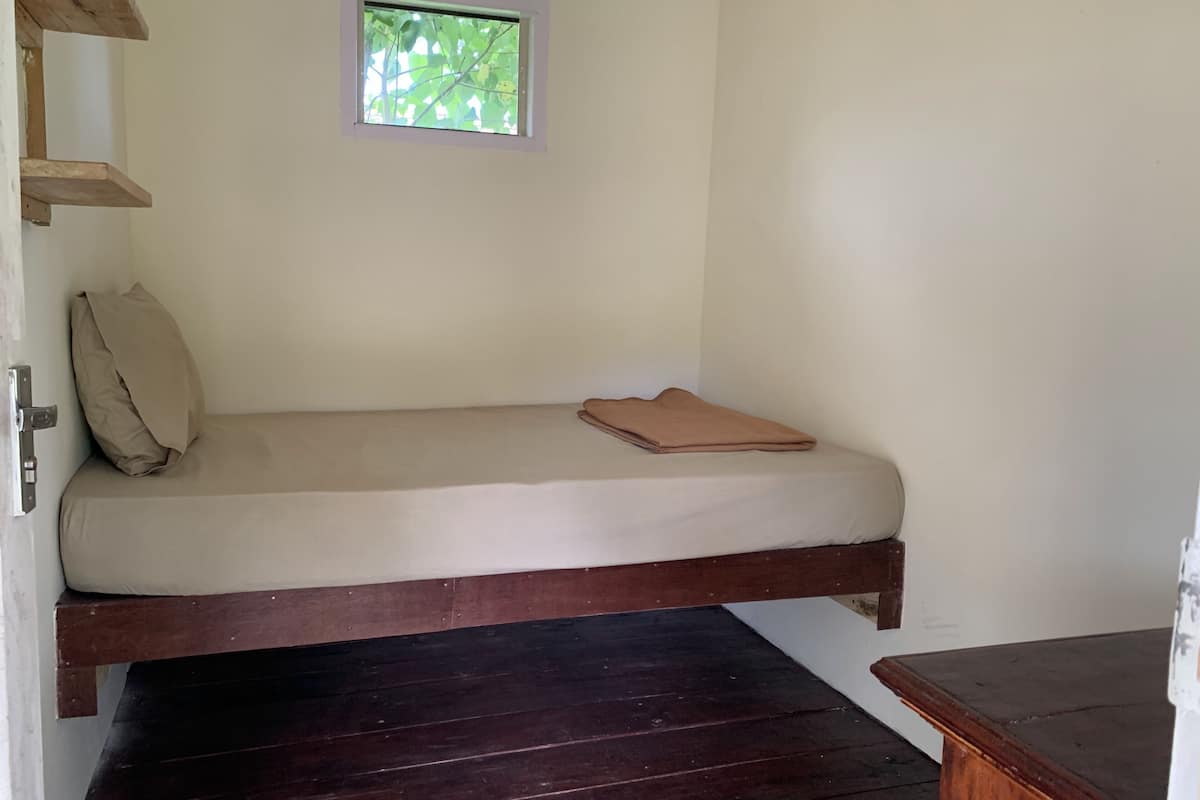Una cama individual con estructura de madera, una ventana pequeña y una puerta.