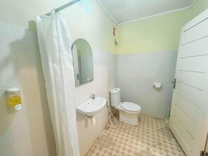 A small bathroom with a shower curtain, a sink, a toilet, and a mirror. - Rinjani Garden Syariah by ecommerceloka (Sembalun Lawang)