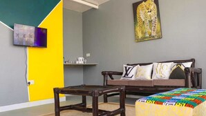Una habitación con sofá, una mesita, un otomano de colores, un televisor montado en la pared y un cuadro de un leopardo.