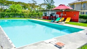 Una piscina con un edificio rojo y sillas de descanso al fondo.