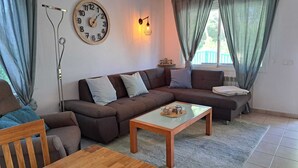 Un salon moderne avec un canapé d’angle, une table basse en bois, une horloge murale et un lampadaire.
