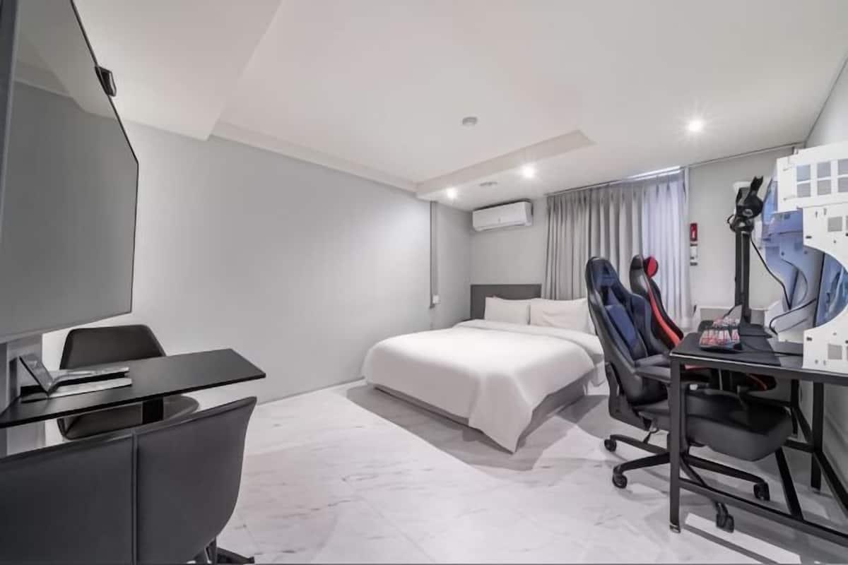 A modern hotel room with a bed, desk, chair, and a TV.